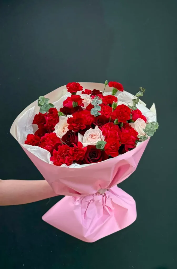 Full view of Orleans Opera bouquet with red carnations, red and blush roses, eucalyptus, and pink wrap