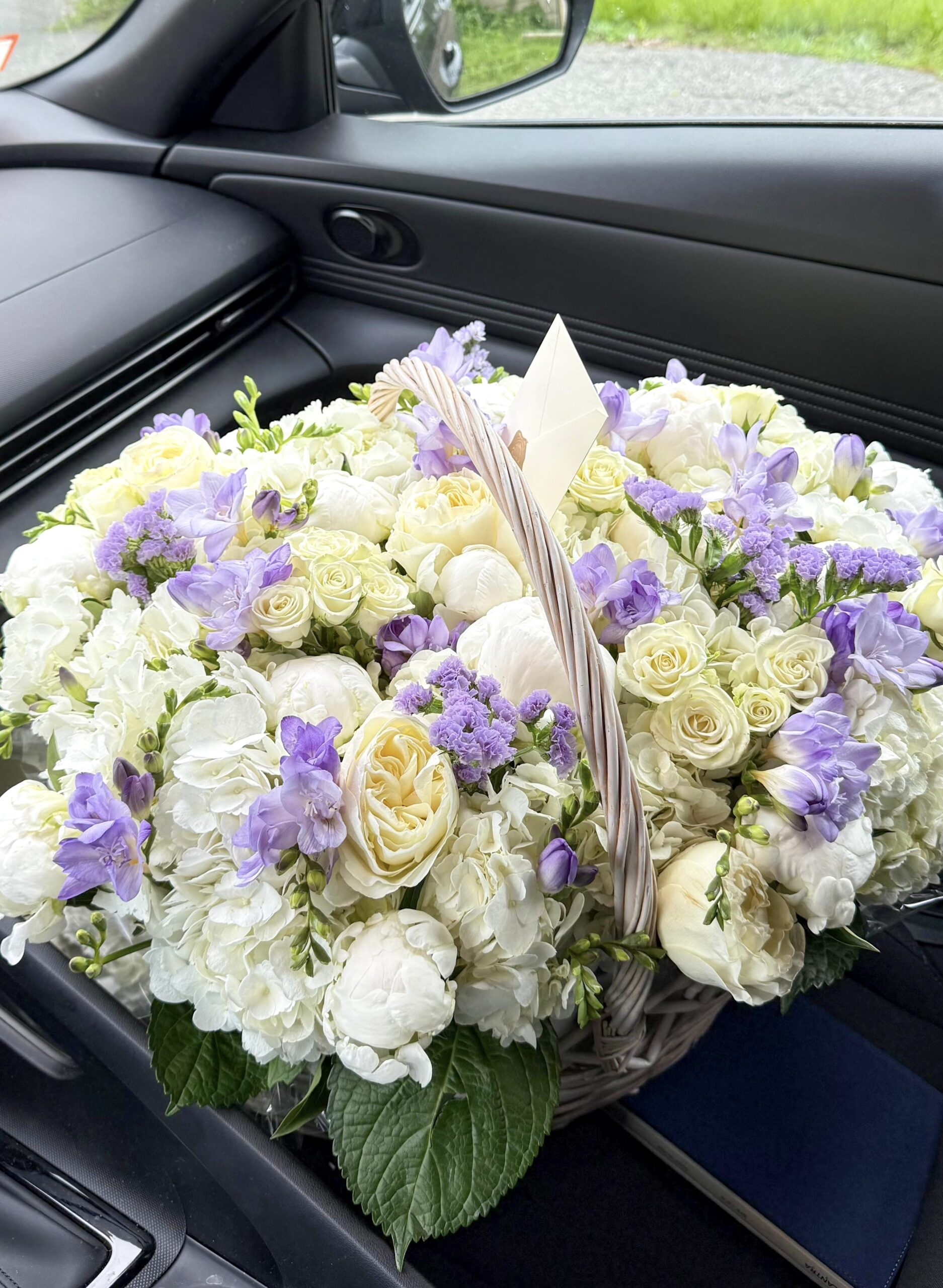 White peonies, roses, hydrangeas and lavender freesia in a woven basket