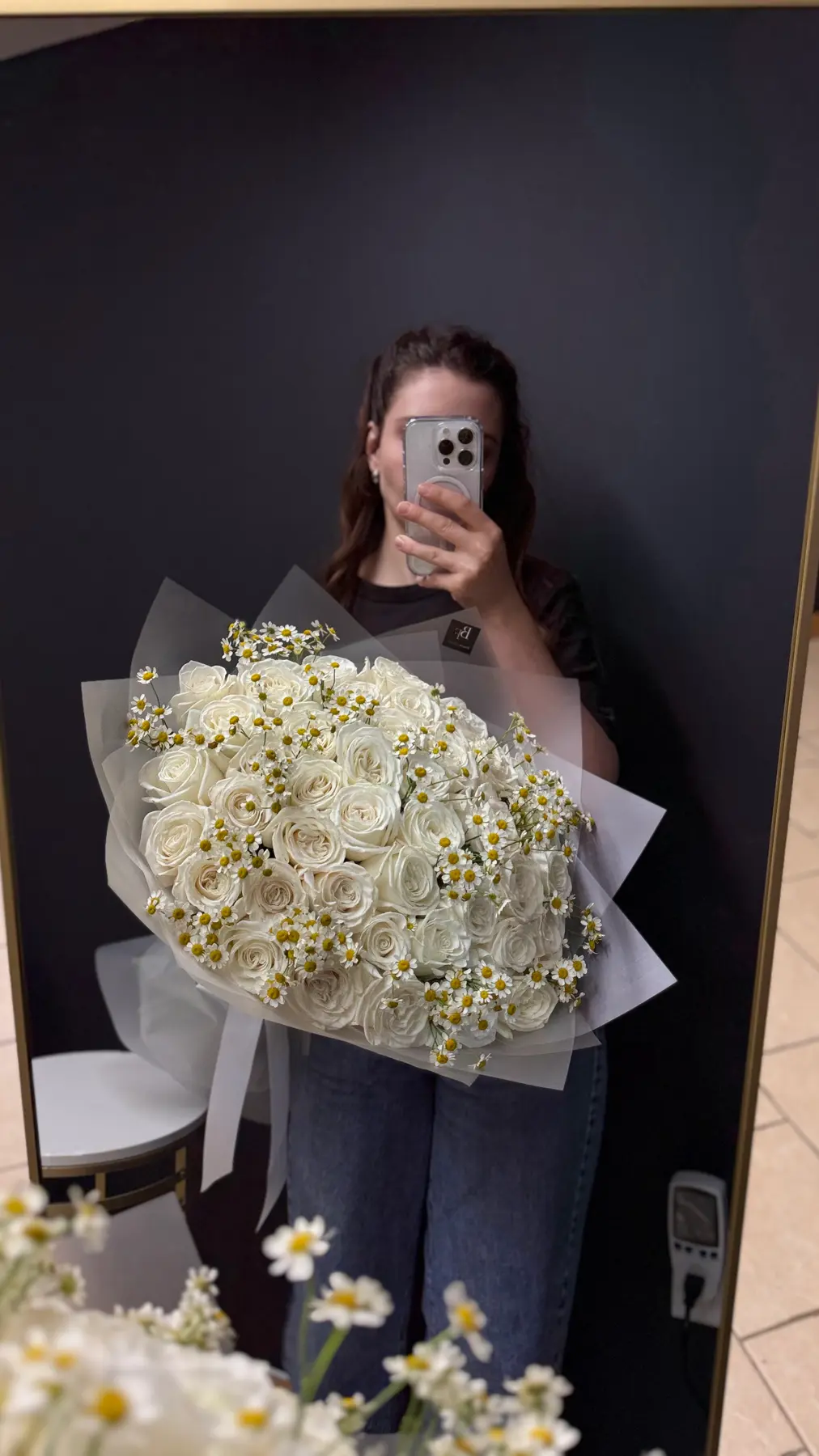 Woman holding a large white rose and chamomile bouquet in gray wrapping