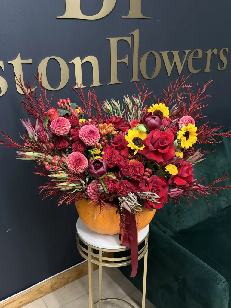 New England Harvest pumpkin flower arrangement with red roses, pink dahlias, sunflowers and burgundy autumn foliage