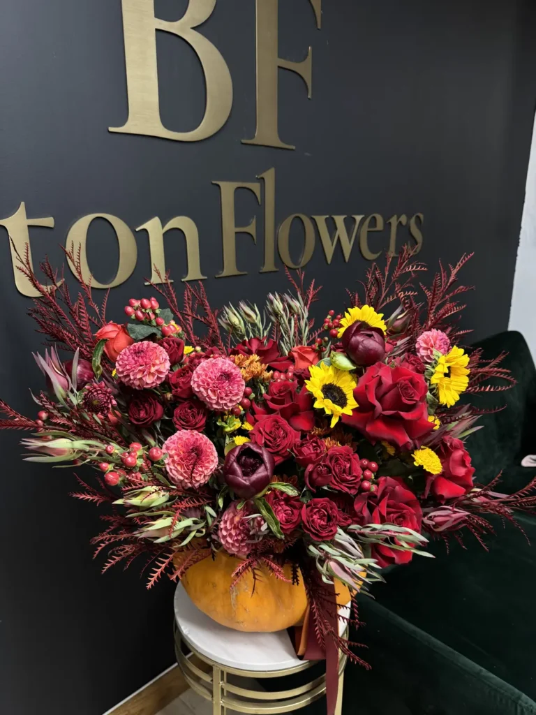 New England Harvest pumpkin flower arrangement with red roses, pink dahlias, sunflowers and burgundy autumn foliage, view 2