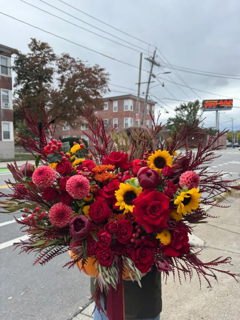 New England Harvest pumpkin flower arrangement with red roses, pink dahlias, sunflowers and burgundy autumn foliage, view 3
